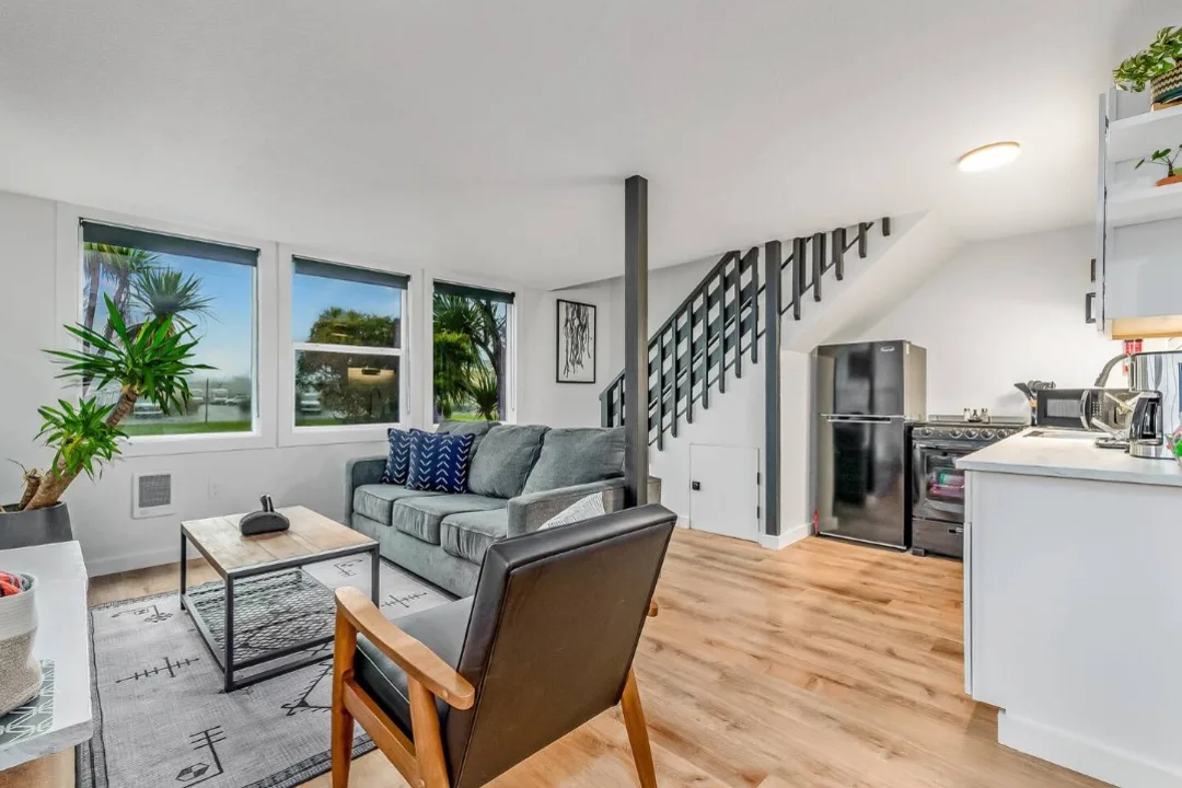 Open living room and kitchen of Tidal House Chalet 7 with a gray sofa, wood flooring, and black staircase.